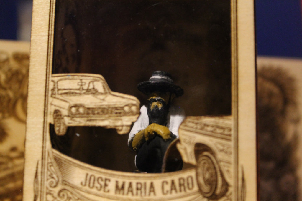 Don Memo
"Fotografía en primer plano de una figura de colección a escala (5-6 cm) de Don Memo, un hombre mayor con sombrero, barba larga, camisa blanca y pantalones oscuros. Está sentado de perfil sobre una silla en miniatura, con las manos cruzadas en su regazo y la mirada hacia el frente, transmitiendo una postura serena y experimentada. La figura, de estilo artesanal y pintada a mano, se encuentra dentro de un nicho de madera grabado."